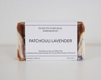 May include: A bar of handmade Patchouli Lavender soap with a white label that reads "TUNETTI NATURAL tunettinatural.com PATCHOULI LAVENDER Olive Pomace, Coconut & Palm Oils Lye, Patchouli & Lavender Essential Oils, Cocoa & Mica Powder, & Vitamin E Handmade in Missouri Net wt 4 oz".