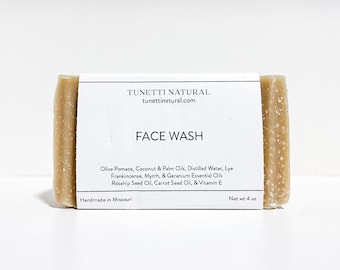May include: A bar of beige soap with a white label that reads "TUNETTI NATURAL tunettinatural.com FACE WASH Olive Pomace, Coconut & Palm Oils, Distilled Water, Lye Frankincense, Myrrh, & Geranium Essential Oils Rosehip Seed Oil, Carrot Seed Oil, & Vitamin E Handmade in Missouri Net wt 4 oz"