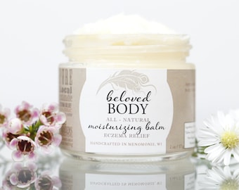May include: A jar of Beloved Body moisturizing balm for eczema relief. The label features the brand name and product details. The jar is surrounded by white flowers and pink flowers. The product is handcrafted in Menomonie, WI.
