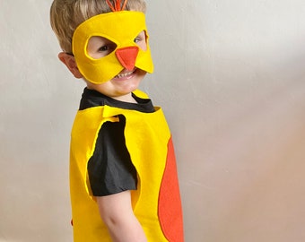Puede incluir: Un niño lleva un disfraz de fieltro amarillo con un círculo rojo en la parte delantera y una máscara de fieltro amarillo con un pico naranja. La máscara tiene un pequeño lazo rojo en la parte superior.