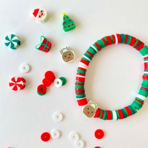 Peut inclure: Un bracelet de Noël composé de perles rondes rouges, vertes et blanches. Le bracelet est orné d'un pendentif en forme de renne et est entouré d'autres pendentifs sur le thème de Noël, notamment une canne en sucre, un sapin de Noël et un Père Noël.