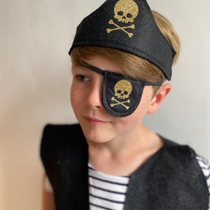 K&ouml;nnte beinhalten: Ein Kind tr&auml;gt ein schwarzes Piratenkost&uuml;m aus Filz mit einem goldenen Augenklappen und einem Stirnband mit Totenkopf und Knochen.