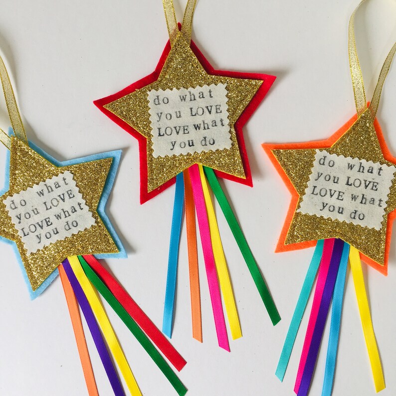 May include: Three star-shaped ornaments in blue, red, and orange, each with gold glitter and a white rectangle with the text "do what you LOVE LOVE what you do." Rainbow ribbons and gold ribbon hangers complete the design.