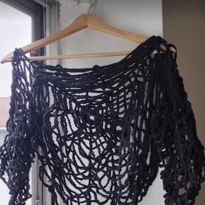 Puede incluir: Top de crochet negro con tejido abierto y suelto. El top est&aacute; colgado en una percha de madera.