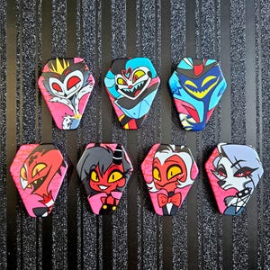 May include: Set of eight pink and black coffin-shaped pins featuring characters from the animated series "Helluva Boss". The characters include:  Lucifer,  Blitzø,  Stolas,  Millie,  Moxxie,  Loona,  and  Fizzarolli.