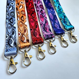 Puede incluir: Seis cordones coloridos con un patrón de ojo repetido y clips giratorios plateados. Los cordones son azul, naranja, rojo, rosa, morado y turquesa.