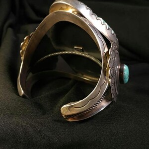 以下が含まれることがあります： ターコイズのアクセントが付いたシルバーのカフブレスレット。ブレスレットは、装飾的なエッジや中央のターコイズストーンなど、複雑な金属細工が特徴です。デザインは、南西部またはネイティブアメリカンの美学を持っています。