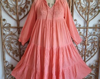 Könnte beinhalten: Ein korallenfarbenes, gestuftes Maxikleid mit langen Ärmeln und einem gerafften Ausschnitt. Das Kleid hat zarte Stickereien am Oberteil.