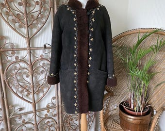 Puede incluir: Abrigo de ante verde oscuro con ribete de piel marrón y detalles bordados. El abrigo se exhibe en un maniquí de madera. El abrigo tiene cierre de botones y bolsillos. El abrigo es de estilo vintage.