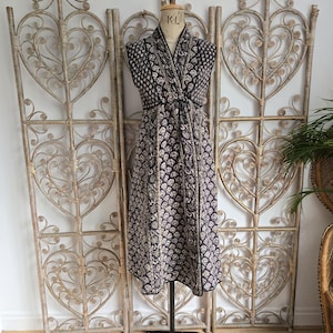 Puede incluir: Un vestido estampado en blanco y negro con escote en V y sin mangas. El vestido se muestra en un maniquí contra una pantalla de mimbre blanca.