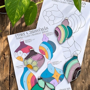 May include: A Funky Christmas Stained Glass Ornament Bundle pattern sheet featuring numbered templates and four finished glass ornaments in shades of pink, teal, and cream with silver metal soldering and hanging loops.