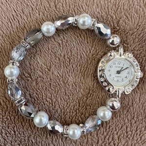Women’s delicate pearl/silver single banded watch with a small face surrounded with rhinestones.