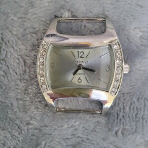 May include: A silver watch with a white face and a silver band. The watch has a crystal-encrusted bezel and the words "Geneva Quartz" on the face.