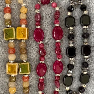May include: Four beaded bracelets in shades of yellow, red, and black. The bracelets feature a variety of beads, including square, round, and oval shapes, with silver accents. The bracelets are connected with silver clasps.