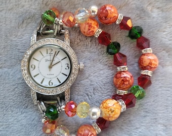 May include: A Geneva Platinum watch with a white face and rhinestone bezel is paired with a beaded bracelet. The bracelet features red, orange, green, and clear beads. The watch has a silver band and a white watch face.