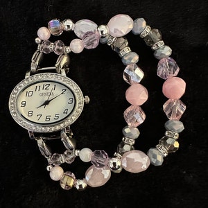 This is a shiny pink/gray interchangeable stretch beaded watch band attached to a smaller, oval, white watch face.