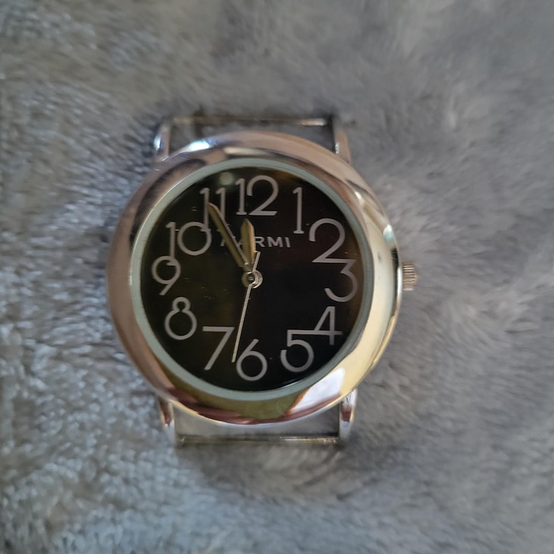 May include: A silver wristwatch with a black face and white numbers. The watch has a silver band.