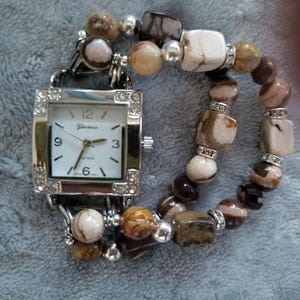 Women’s lovely brown and white stretch interchangeable watch bracelet with a white watch face with rhinestones in each of the corners.