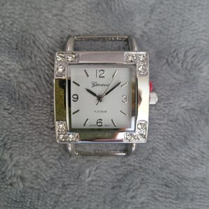 May include: A silver square watch with a white face and rhinestones around the bezel. The watch face has black hands and black Roman numeral hour markers. The watch face also has the words "Geneva" and "Platinum" printed on it.