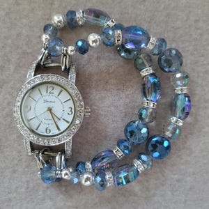 This iridescent blue ladies interchangeable stretch beaded watch has a variety of iridescent beads with a round watch face with rhinestones.