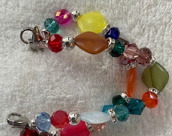 May include: A colorful beaded bracelet featuring a variety of shapes and colors, including red, pink, yellow, blue, and green. The bracelet has silver-tone metal clasps and accents, with some beads embellished with rhinestones.