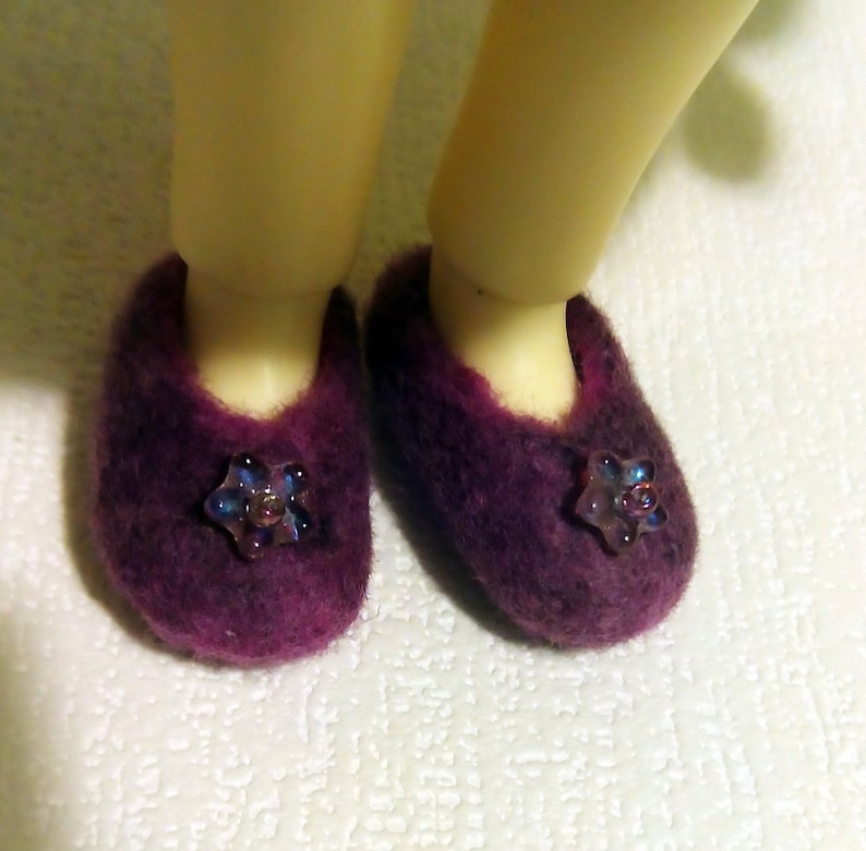 May include: A pair of purple fuzzy slippers with a flower-shaped embellishment on each.
