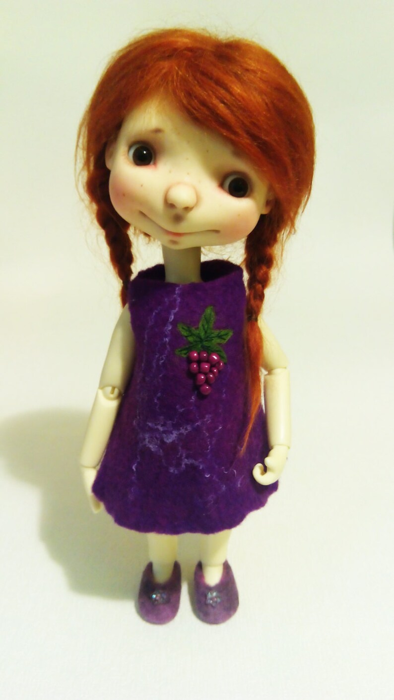 May include: A doll with red hair wearing a purple dress with a grape design. The doll is wearing purple shoes.