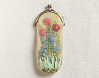 May include: A small, cream-coloured felt coin purse with a metal clasp. The purse is decorated with embroidered flowers in shades of pink, blue, and green.