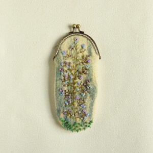 May include: A small, white felt pouch with a floral embroidery design. The pouch has a brass clasp and is decorated with green beads.