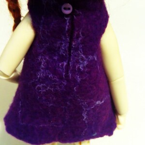 May include: A purple felt dress with a button closure in the back. The dress is worn by a doll with red hair.