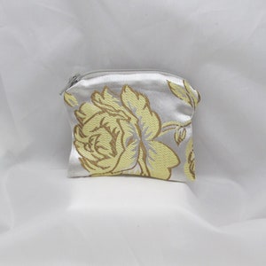 May include: A small, white satin coin purse with a zipper closure. The purse is decorated with a yellow floral pattern.