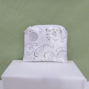 May include: A white zippered pouch with a silver floral pattern.