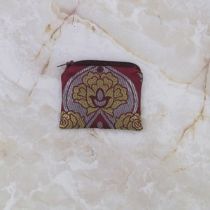 May include: A small red zippered pouch with a gold and silver floral pattern.