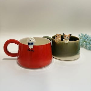 Peut inclure: Deux mugs en céramique avec des figurines de chiens. Un mug rouge avec une figurine de chien blanc et le nom "Benny". L'autre mug est vert avec deux figurines de chiens. Les mugs ont une anse arrondie et un intérieur blanc.