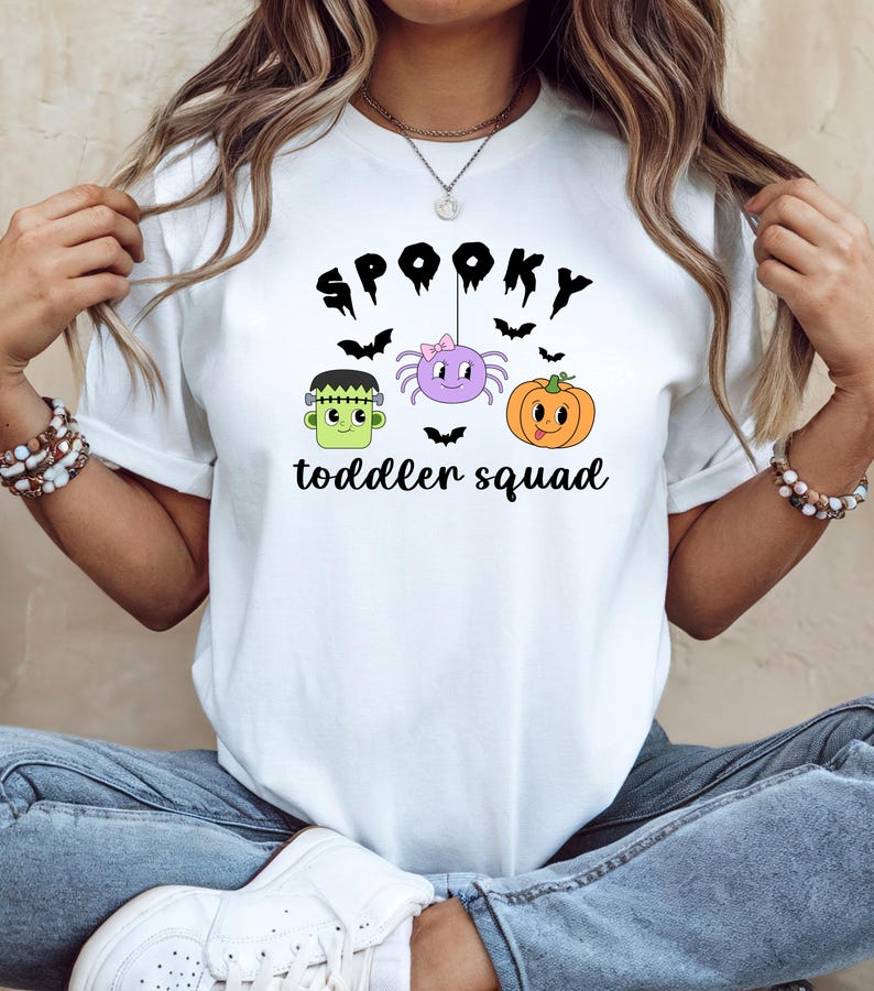 Peut inclure: T-shirt blanc avec un motif sur le th&egrave;me d'Halloween. Le motif comprend le texte "Spooky toddler squad" avec des illustrations d'un monstre de Frankenstein, d'une araign&eacute;e, d'une citrouille et de chauves-souris.
