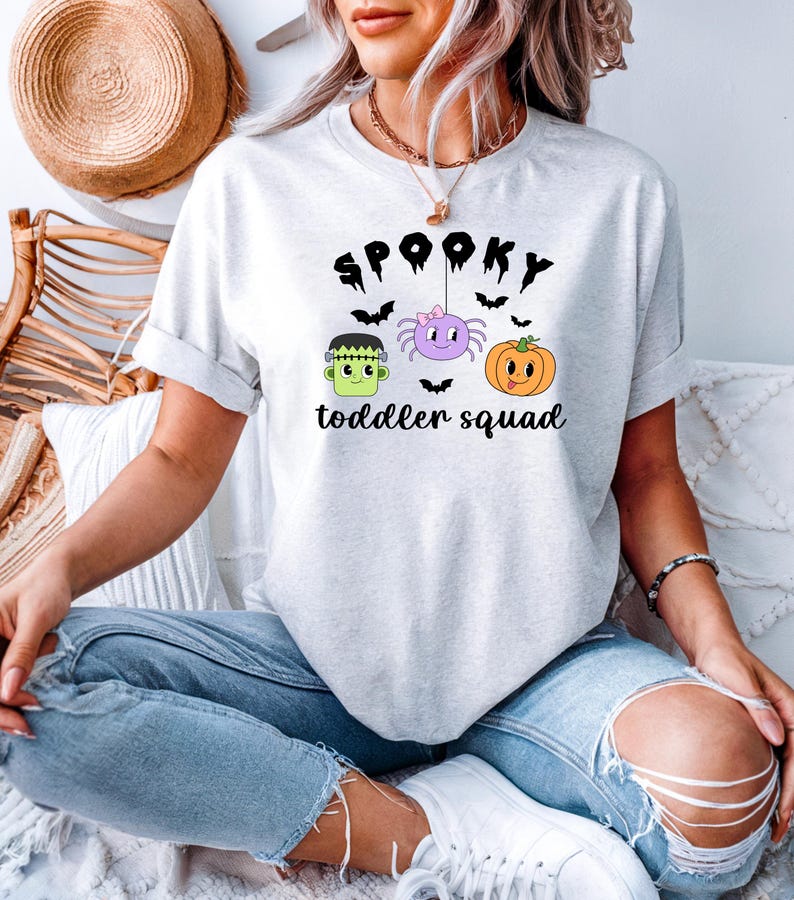 Peut inclure: T-shirt gris clair avec un motif sur le th&egrave;me d'Halloween. Le motif comprend le mot "Spooky" au-dessus d'un dessin anim&eacute; de Frankenstein, d'une araign&eacute;e et d'une citrouille. Le texte "toddler squad" est en dessous. Le t-shirt est en mati&egrave;re douce.