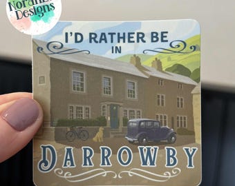 May include: Square sticker featuring the text "I'd Rather Be In Darrowby" above a detailed illustration of a house, car, bicycle, and dog. The sticker has a watercolor design with the NorahLu Designs logo in the upper left corner.
