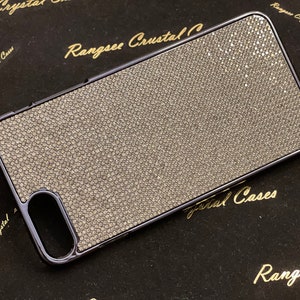 May include: A black phone case with a sparkly, silver, textured surface. The case has a raised edge around the camera lens and a cutout for the charging port. The case is on a black surface with the text "Rangsee Crystal" printed in gold.