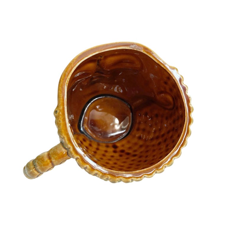 May include: A top-down view of a brown ceramic mug with a glossy finish. The interior features a textured, dimpled pattern along the lower walls, while the upper rim is smooth. A sturdy, segmented handle extends from the side of the round vessel.