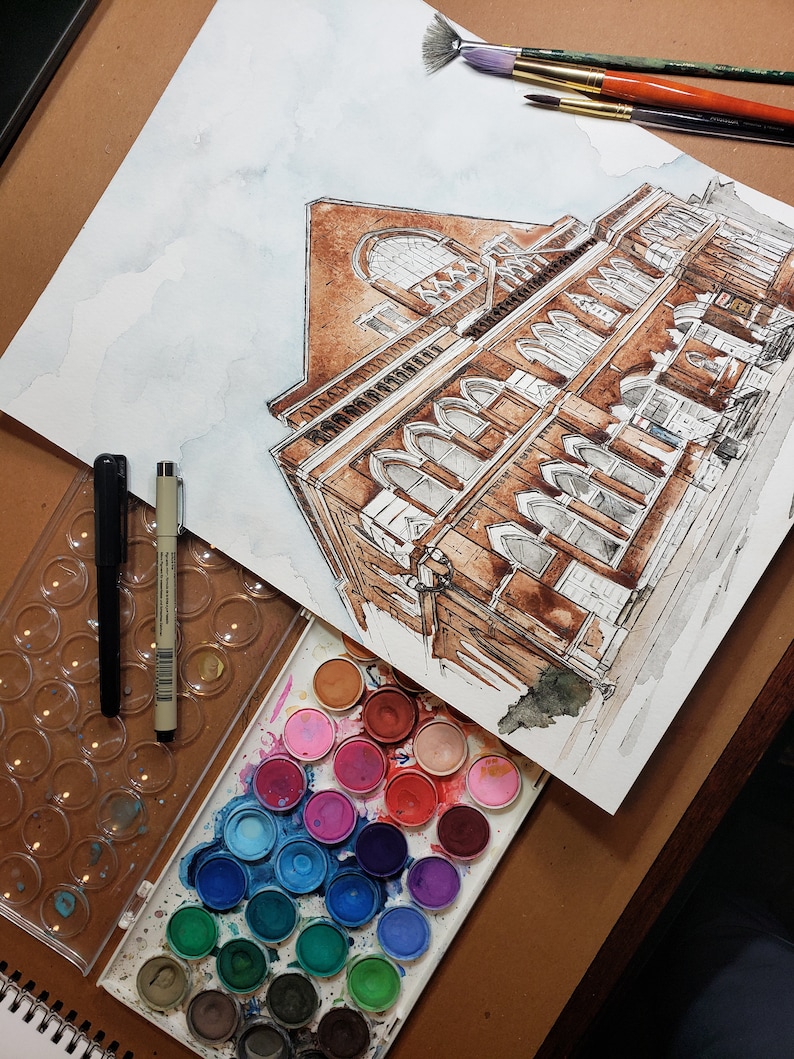 Puede incluir: Una pintura de acuarela de un edificio con una fachada de ladrillo marr&oacute;n y muchas ventanas. La pintura est&aacute; en una hoja de papel blanco y est&aacute; rodeada de una variedad de pinturas de acuarela.