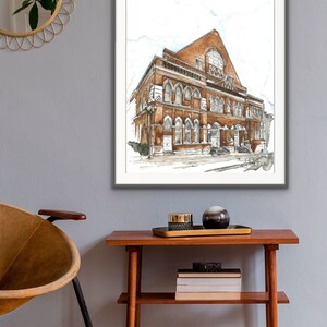Puede incluir: Una ilustraci&oacute;n de acuarela de un edificio de ladrillo con ventanas arqueadas y una gran ventana redonda. El edificio est&aacute; enmarcado en un marco gris y cuelga de una pared gris.