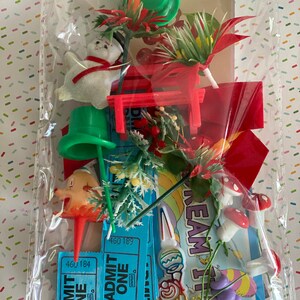 May include: A clear plastic bag filled with various vintage Christmas and carnival-themed decorations. Includes a snowman, red bench, green top hats, mushrooms, and blue "Admit One" tickets. A festive assortment of colorful, miniature ornaments.