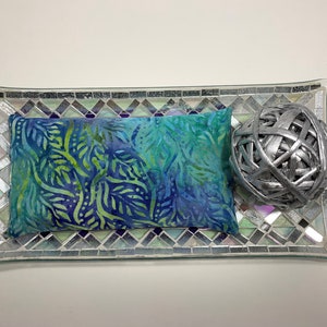 May include: A blue and green patterned eye pillow on a silver mosaic tray with a silver decorative ball.