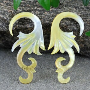 Può includere: Un paio di dilatatori per orecchie in conchiglia gialla e bianca con un design a forma di drago. I dilatatori sono realizzati in conchiglia naturale e hanno un design unico e intricato.