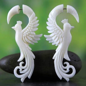 Puede incluir: Un par de pendientes de pájaro tallados en blanco roto. Cada pendiente presenta un pájaro con las alas extendidas y una parte superior curva en forma de media luna. Los pájaros tienen plumas detalladas y una cola decorativa.
