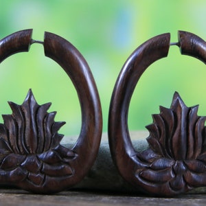 Puede incluir: Un par de pendientes de madera marrón oscuro con un diseño de flor de loto tallada. Los pendientes tienen forma de media luna y un acabado liso y pulido.