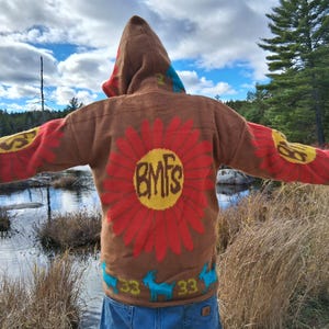 May include: Brown hooded sweater with a large red flower design on the back, featuring the letters "BMFs" in yellow. The sleeves have yellow and red flower designs. Blue and yellow accents are visible.