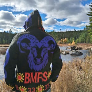 May include: Black hooded sweater with a large purple ram's head design on the back. The sweater also features the letters "BMFS" in red with yellow and red flower accents and the number "33".
