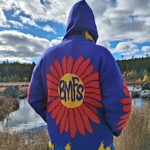 May include: A blue hooded sweater with a large red and yellow flower design on the back, featuring the letters "BMFs". The sweater also has yellow goat graphics and the number "33".