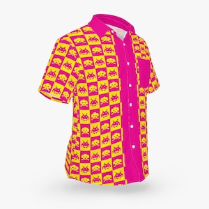 May include: A short-sleeved button-up shirt with a vibrant pink and yellow pixelated pattern. The design features a repeating pattern of yellow pixelated alien figures on a pink checkered background. The shirt has a pocket and a classic collar.